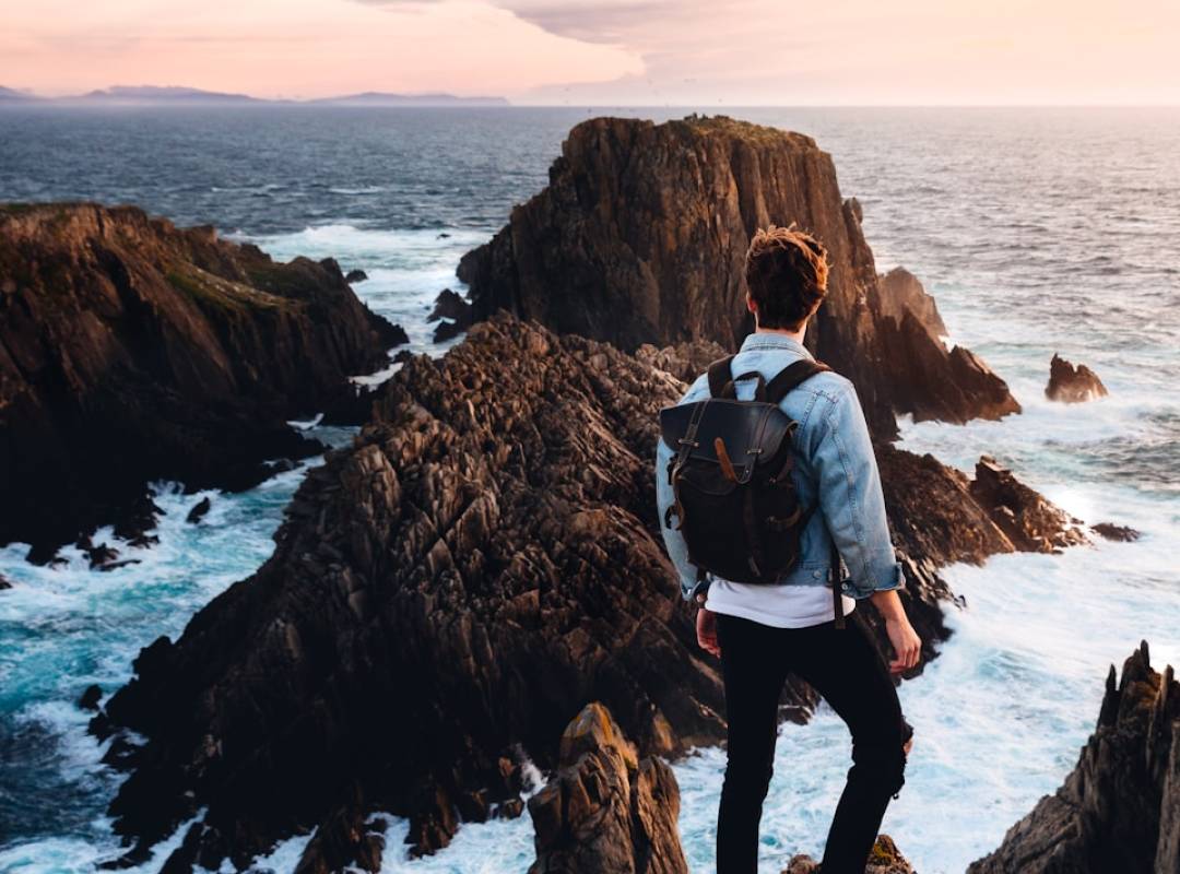 man standing near cliff looking at body of water during daytime